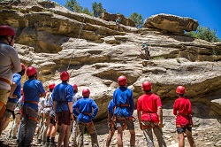 A crew watching as two staff members demonstrate a route on the natural rock of Chase Cow Camp in its first season..   Philmont maintains three rock climbing venues ... Dean Cow was closed due to the Ute Park Fire and Chase Cow was created to take its place starting in 2019 along with Miner's Park and Cimarroncito.